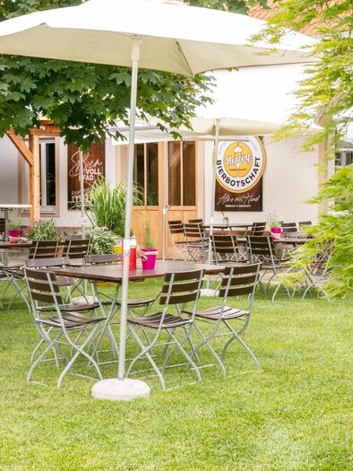 An inviting outdoor area with a table and chairs under a sunshade. Surrounded by greenery and plants.