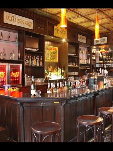 Eine gemütliche Bar mit dunklem Holzinterieur und einer langen Theke. Regale mit verschiedenen Getränken sind sichtbar, ergänzt durch stimmungsvolle Beleuchtung. | © Hubmann