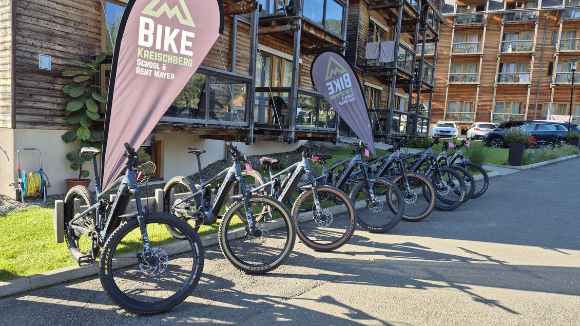 Eine Reihe von Fahrrädern steht an einem modernen Gebäude. Mehrere Fahnen mit dem Schriftzug „Bike“ sind sichtbar. | © TVB Murau