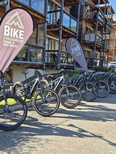 Eine Reihe von Fahrrädern steht an einem modernen Gebäude. Mehrere Fahnen mit dem Schriftzug „Bike“ sind sichtbar. | © TVB Murau