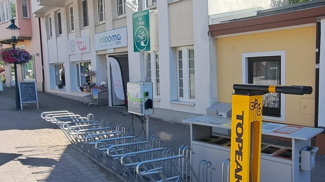 Ein Gebäude mit mehreren Fenstern und einer auffälligen gelben Fahrradverleihstation. Im Vordergrund stehen Einkaufswagen an einem gepflasterten Gehweg.