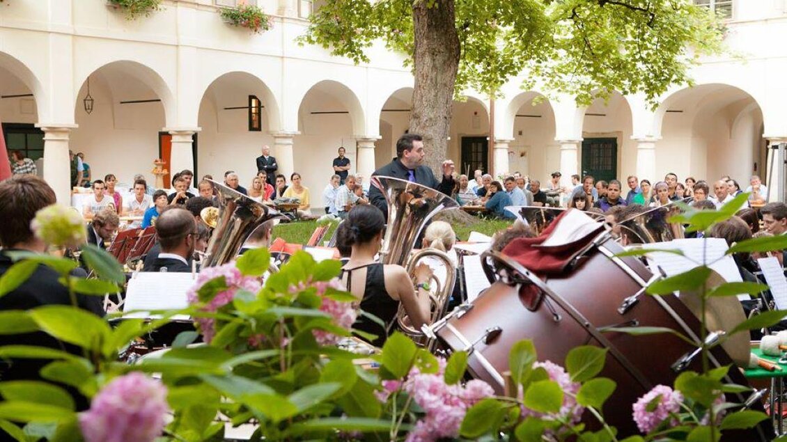 Ein Konzert im Innenhof mit vielen Musikern und einer großen Zuhörerschaft. Bunte Blumen umgeben die Bühne und schaffen eine festliche Atmosphäre. | © Retzhof