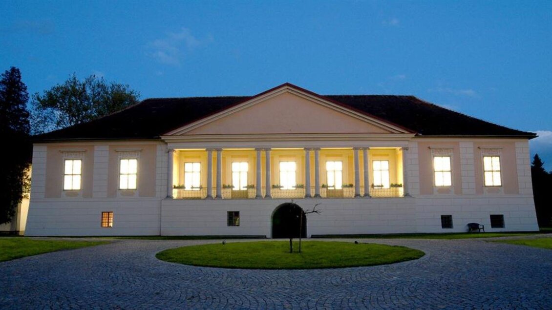 Ein elegantes Gebäude mit großen Fenstern, das sanft beleuchtet ist. Der Himmel ist dunkelblau und der Außenbereich ist grün und gepflegt. | © Retzhof