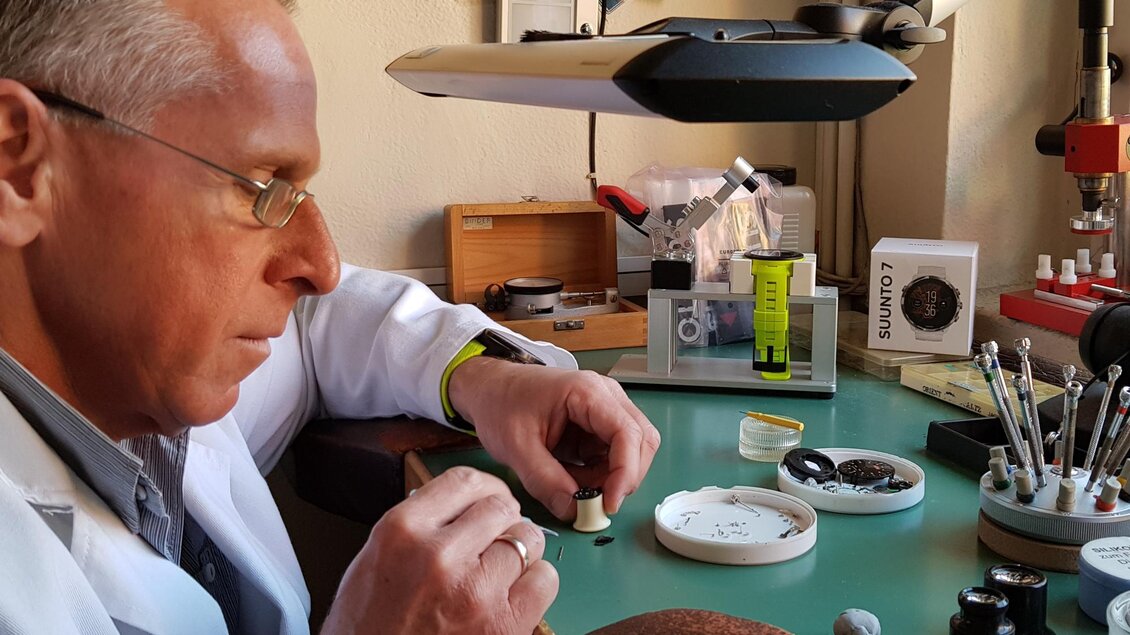Ein Uhrmacher arbeitet konzentriert an einem Zeitmesser. Auf dem Tisch sind verschiedene Werkzeuge und Uhrenkomponenten zu sehen. | © Heinz Michalka