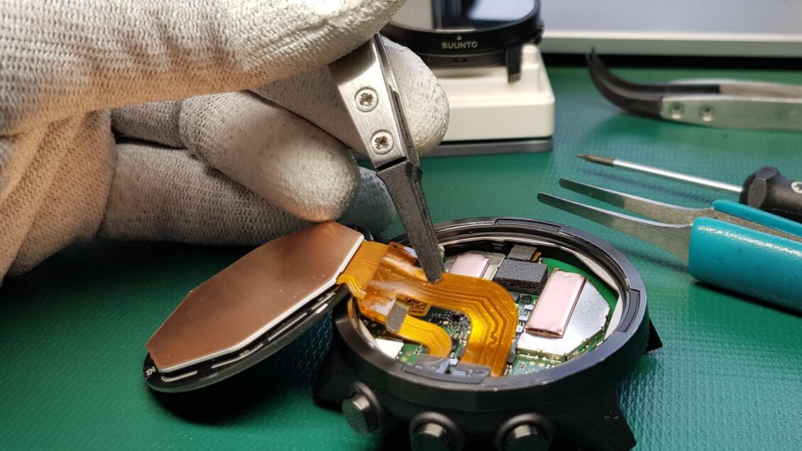 Eine Hand mit einer Pinzette arbeitet an der Innenseite einer Uhr. Das Gehäuse ist geöffnet und zeigt die elektronischen Komponenten. | © Heinz Michalka