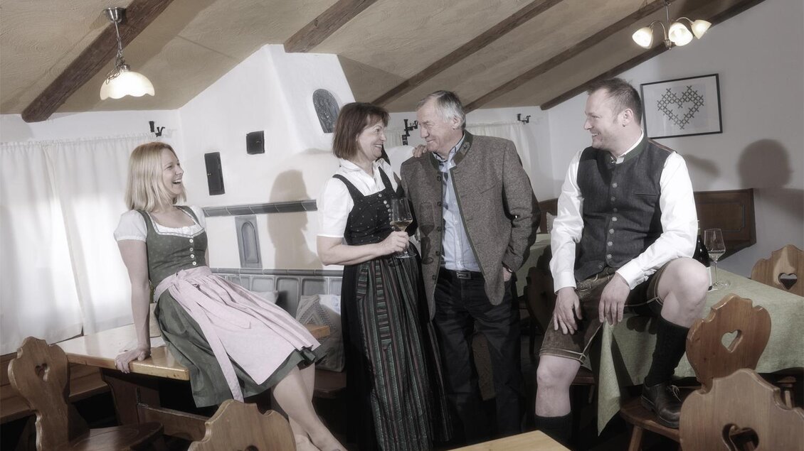 Eine Gruppe von vier Personen trägt traditionelle bayerische Trachten in einem gemütlichen Gastraum. Die Atmosphäre ist freundlich und einladend. | © www.michilorenz.at