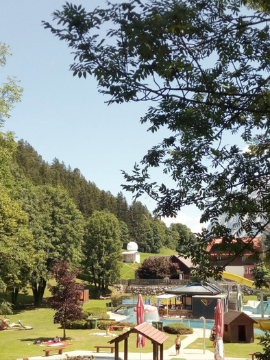Eine grüne Parklandschaft mit Bäumen und einem Spielplatz im Hintergrund. Im Vordergrund sind Liegen und Spielmöglichkeiten zu sehen. | © Johanna Provatopoulos