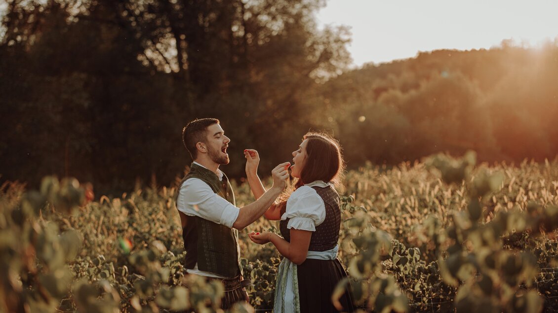Ein Paar steht in einem Weinberg während des Sonnenuntergangs. Sie lachen und teilen einen fröhlichen Moment miteinander. | © Freilichtmomente