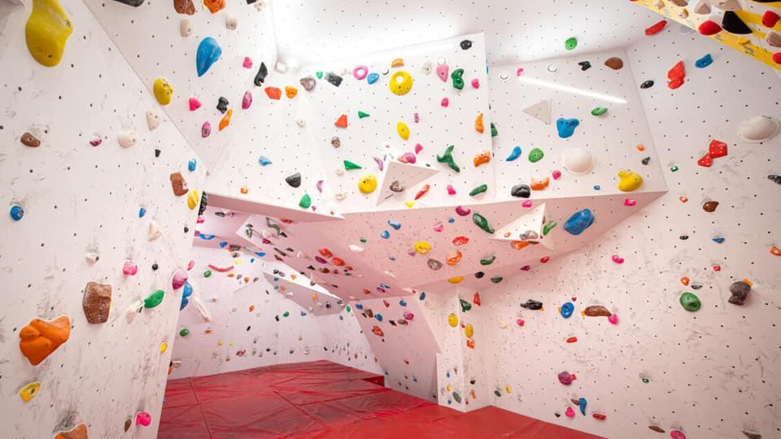Ein moderner Bouldersaal mit bunten Griffen an weißen Wänden. Die rote Matte bietet Sicherheit beim Klettern. | © Christoph Huber