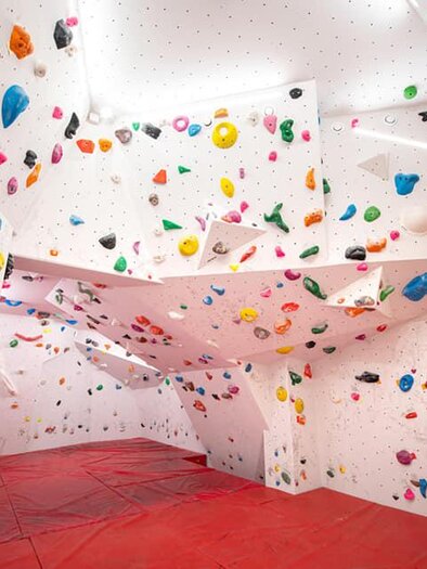 Ein moderner Bouldersaal mit bunten Griffen an weißen Wänden. Die rote Matte bietet Sicherheit beim Klettern. | © Christoph Huber