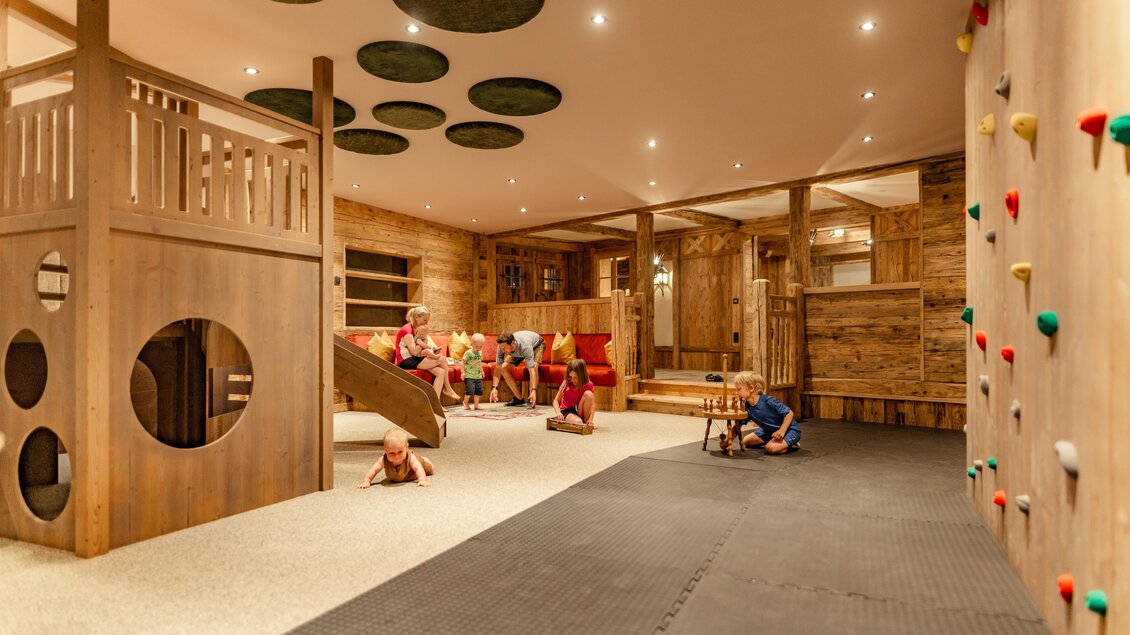 Ein geräumiger Spielbereich aus Holz mit Kletterwand und Rutsche. Kinder spielen und erkunden die verschiedenen Aktivitäten im Raum.