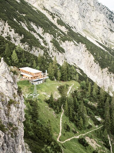 Ein malerisches Bergpanorama mit steilen Felsen und grünen Wäldern. Im Vordergrund steht eine Berghütte, umgeben von Wanderwegen. | © Stefan Leitner