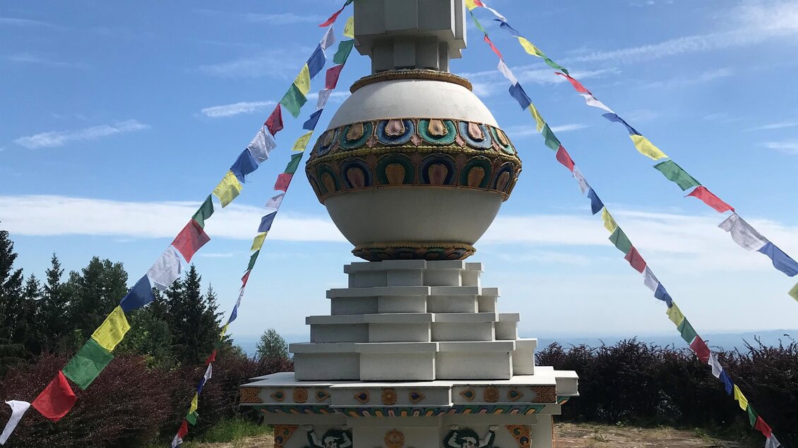 Ein schöner Stupa mit bunten Gebetsfahnen steht auf einer Wiese. Der Himmel ist blau und leicht bewölkt. | © Alexandra Wippel
