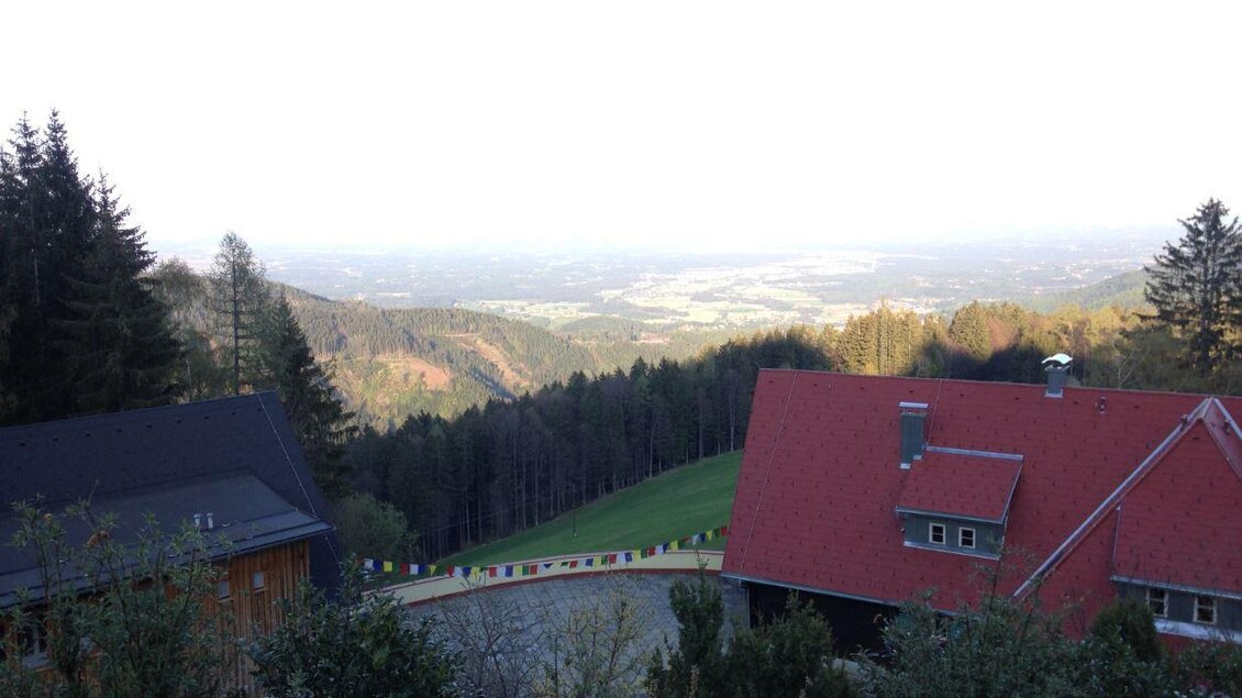 Eine malerische Aussicht auf das Tal mit sanften Hügeln und einem klaren Himmel. Im Vordergrund sind zwei Häuser, umgeben von Bäumen und Natur. | © TV Sulmtal Koralm