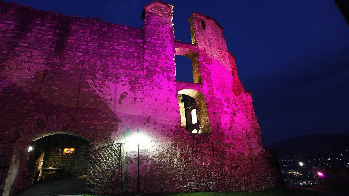 Eine alte Ruine, die nachts beleuchtet ist, erstrahlt in pinken und lila Tönen. Der Himmel ist dunkel, und im Hintergrund sind Lichter der Stadt sichtbar. | © Enrico Caracciolo