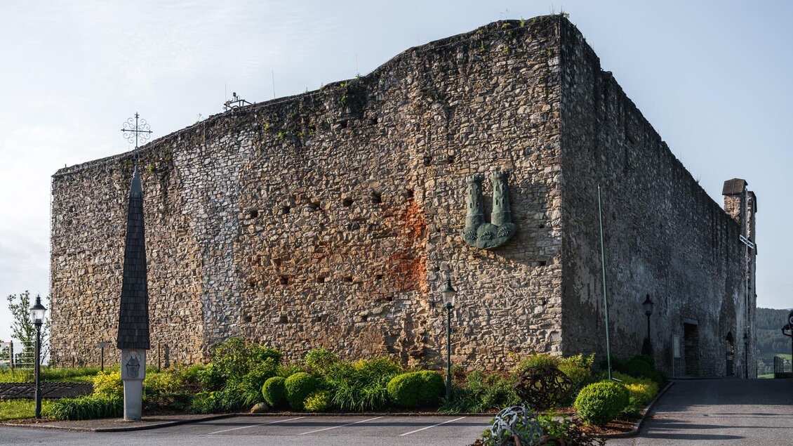 <p>Massive Steinmauer der Burgruine Obervoitsberg mit Grünflächen und Blumen im Vordergrund | © Bernd Grosseck