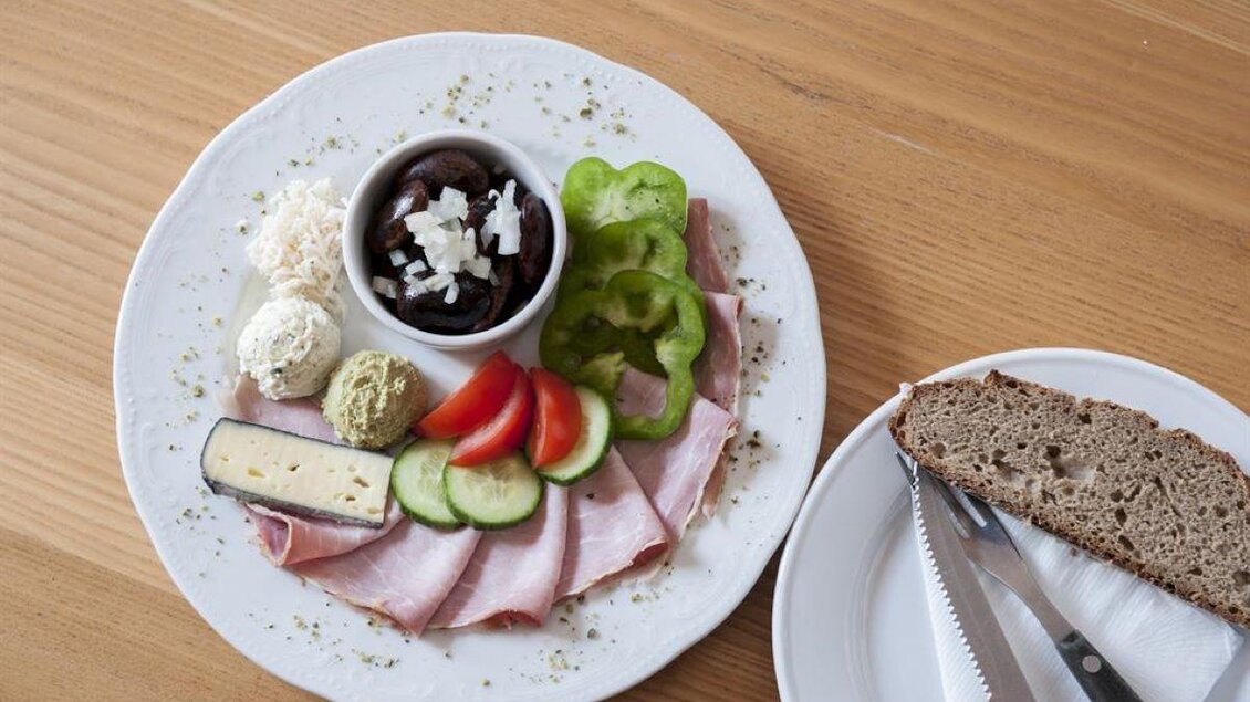 Ein Teller mit Aufschnitt, frischem Gemüse und verschiedenen Käsesorten. Dazu liegt ein Stück Brot auf einem separaten Teller. | © Weingut Assigal