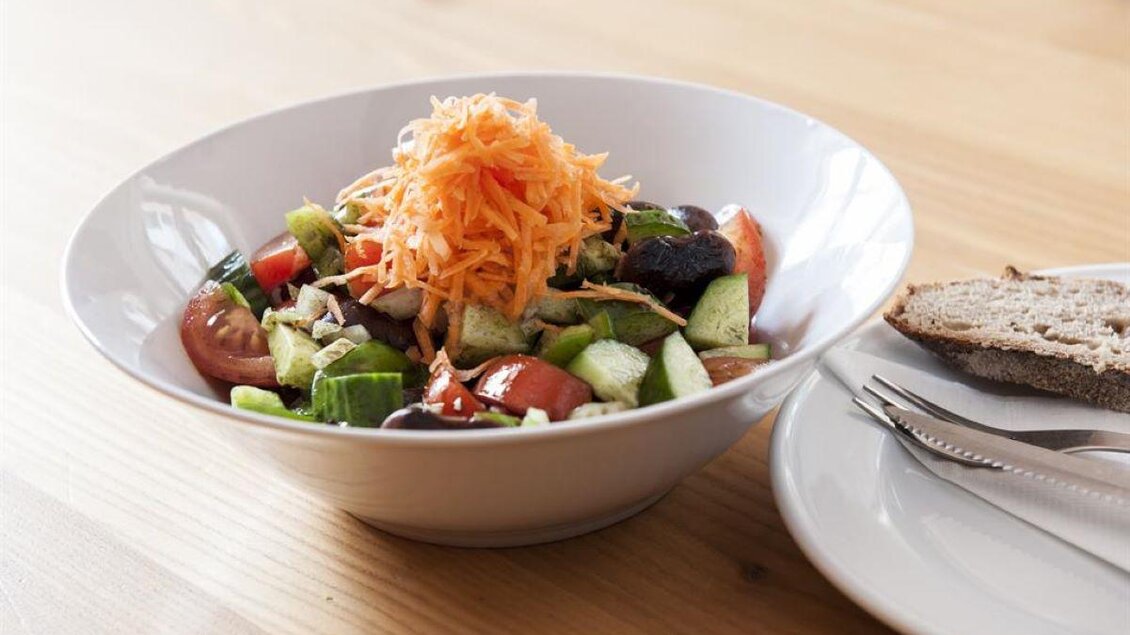 Ein frischer Salat mit Tomaten, Gurken, und geraspelter Karotte. Daneben liegt eine Scheibe Brot auf einem Teller. | © Weingut Assigal