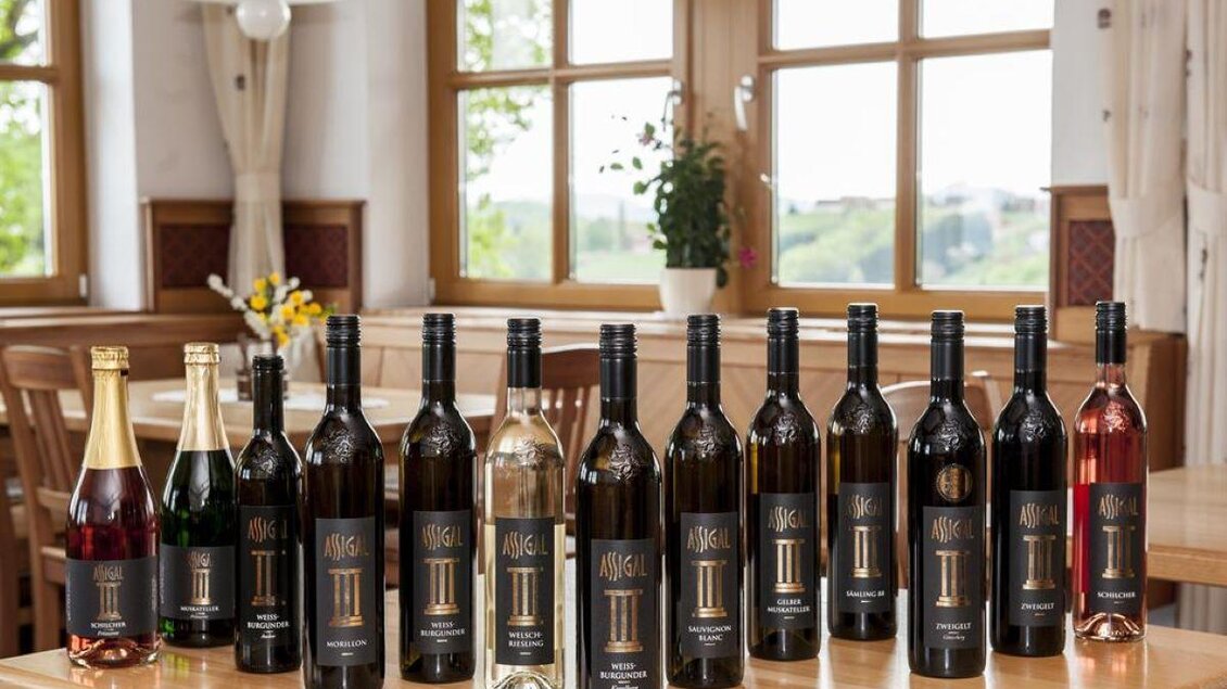 Eine Auswahl an Weinen in verschiedenen Flaschen auf einem Tisch. Im Hintergrund sind Fenster mit Blick auf die Natur. | © Weingut Assigal