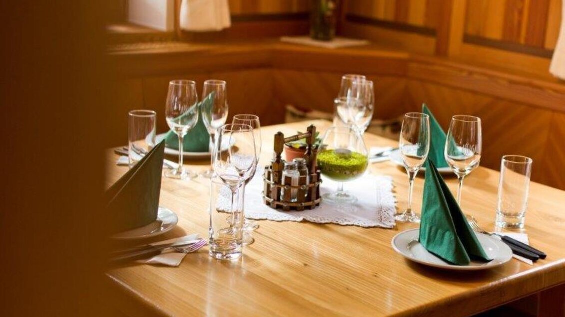 Ein gedeckter Tisch in einem gemütlichen Restaurant. Grüne Servietten und Gläser schaffen eine einladende Atmosphäre. | © Weingut Assigal