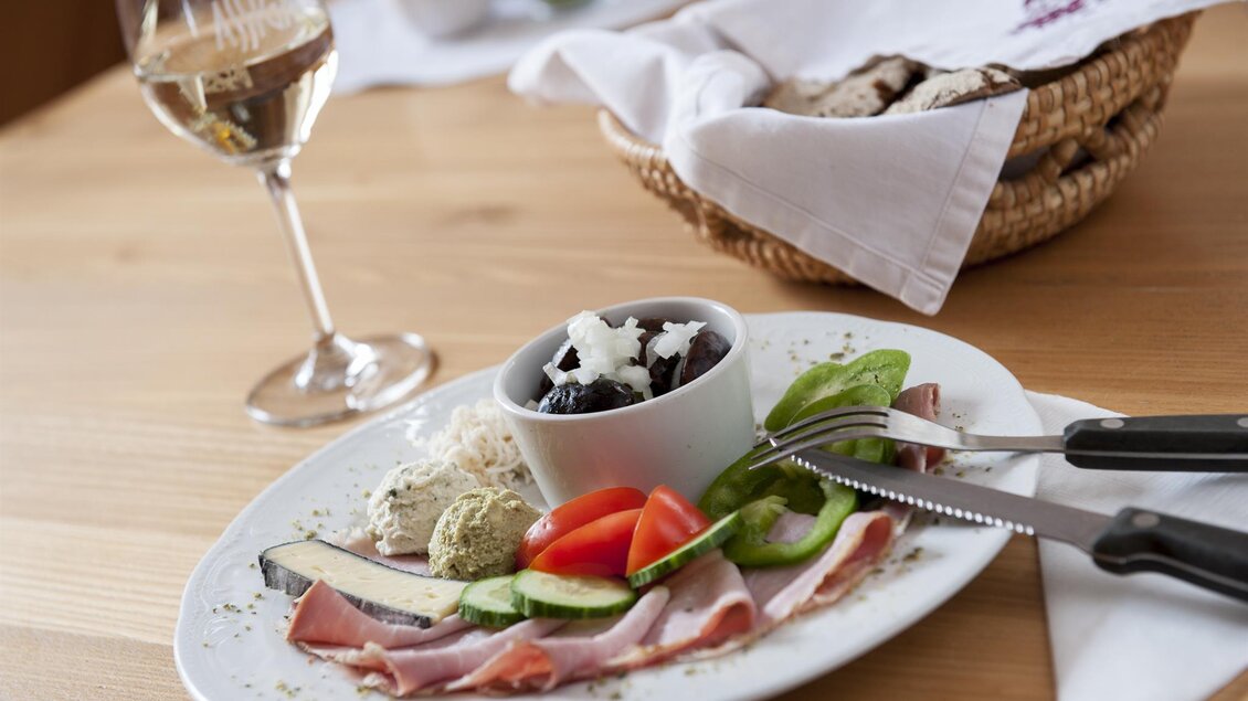 Ein Teller mit Wurst, Käse und frischem Gemüse. Dazu ein Glas Weißwein und ein Körbchen mit Brot. | © Weingut Assigal