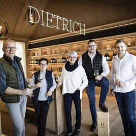 Eine Gruppe von fünf Personen steht in einem modernen Weingeschäft. Im Hintergrund sind Holzregale mit Weinflaschen und der Schriftzug "DIETRICH" zu sehen. | © BU Dietrich