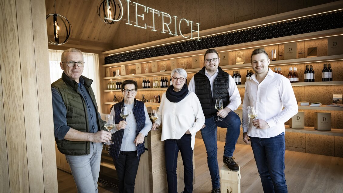 Eine Gruppe von fünf Personen steht in einem modernen Weingeschäft. Im Hintergrund sind Holzregale mit Weinflaschen und der Schriftzug "DIETRICH" zu sehen. | © BU Dietrich