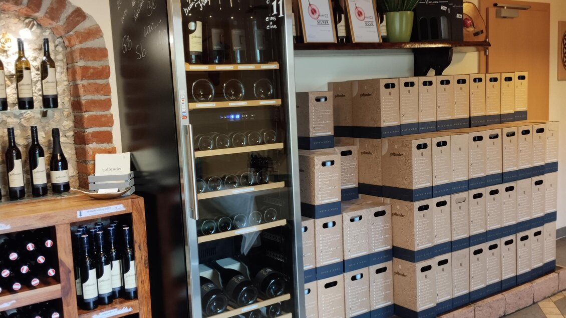 Ein gut ausgestatteter Weinkeller mit einem Kühlschrank für Wein und Holzregalen. Auf der rechten Seite sind viele Kisten mit Wein verpackt.