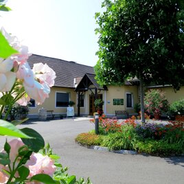 Ein charmantes Gebäude umgeben von blühenden Blumen und grünen Pflanzen. Der Eingang ist einladend und die Atmosphäre ist freundlich. | © Stefan Gründl | Weingut Gründl