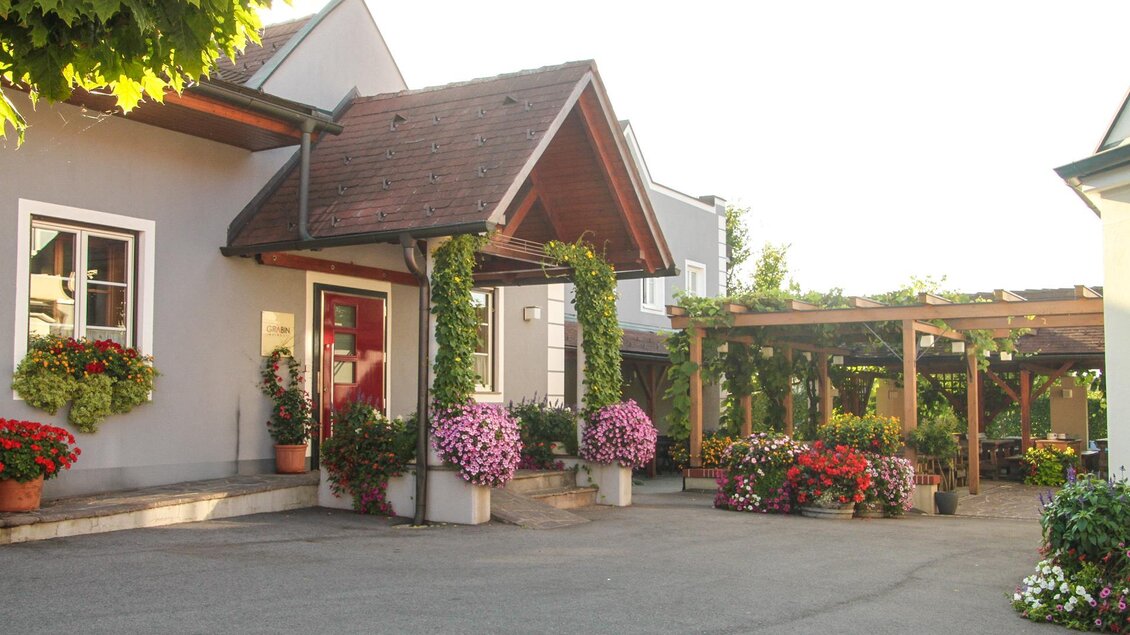 Ein einladendes Gebäude mit einem blühenden Eingangsbereich. Bunte Blumen und ein gepflasterter Hof schaffen eine gemütliche Atmosphäre. | © Weingut Grabin