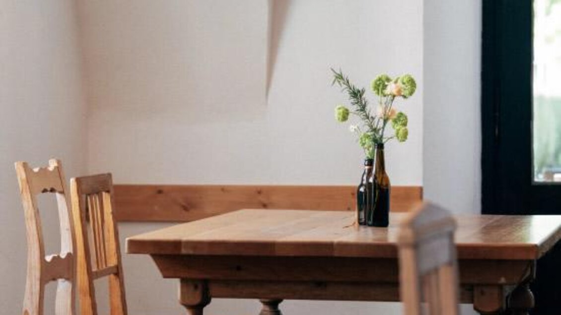Ein gemütliches Restaurant mit einem Holztisch und Stühlen. Auf dem Tisch steht eine Vase mit frischen Blumen. | © Heldentheater
