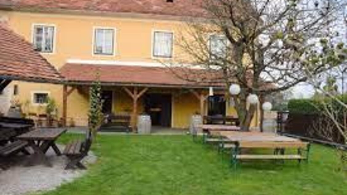 Ein gemütliches Haus mit einem gelben Anstrich und einem roten Dach. Im Vordergrund befindet sich ein schöner Garten mit Sitzgelegenheiten und einem Baum. | © Buschenschank Habersack