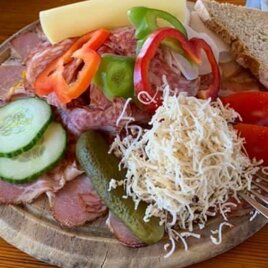 Eine appetitliche Platte mit Wurst, Käse, frischem Gemüse und Brot. Dazu gehören Gurken, Tomaten, Paprika und ein Salat aus Käse. | © Häuser am Wald | T. Hartner