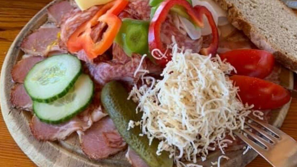 Eine appetitliche Platte mit Wurst, Käse, frischem Gemüse und Brot. Dazu gehören Gurken, Tomaten, Paprika und ein Salat aus Käse. | © Häuser am Wald | T. Hartner