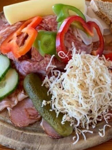 Eine appetitliche Platte mit Wurst, Käse, frischem Gemüse und Brot. Dazu gehören Gurken, Tomaten, Paprika und ein Salat aus Käse. | © Häuser am Wald | T. Hartner