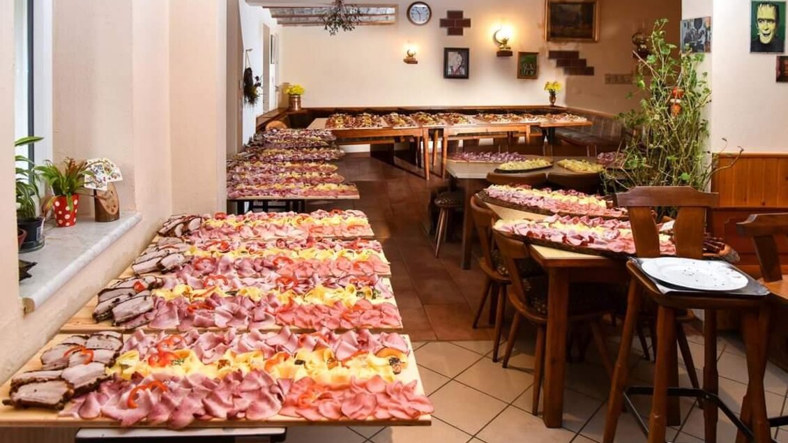 Ein gemütlicher Raum mit langen Tischen, die mit einer Vielzahl von Fleisch- und Käseplatten gedeckt sind. Die Atmosphäre ist einladend und geschmackvoll. | © Buschenschank Heschl