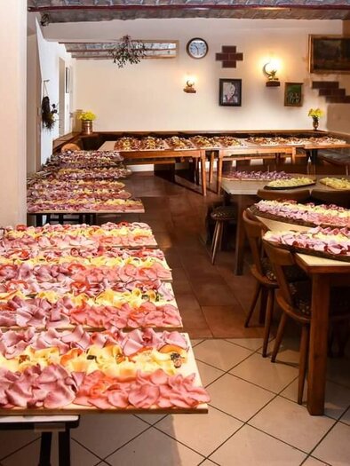 Ein gemütlicher Raum mit langen Tischen, die mit einer Vielzahl von Fleisch- und Käseplatten gedeckt sind. Die Atmosphäre ist einladend und geschmackvoll. | © Buschenschank Heschl