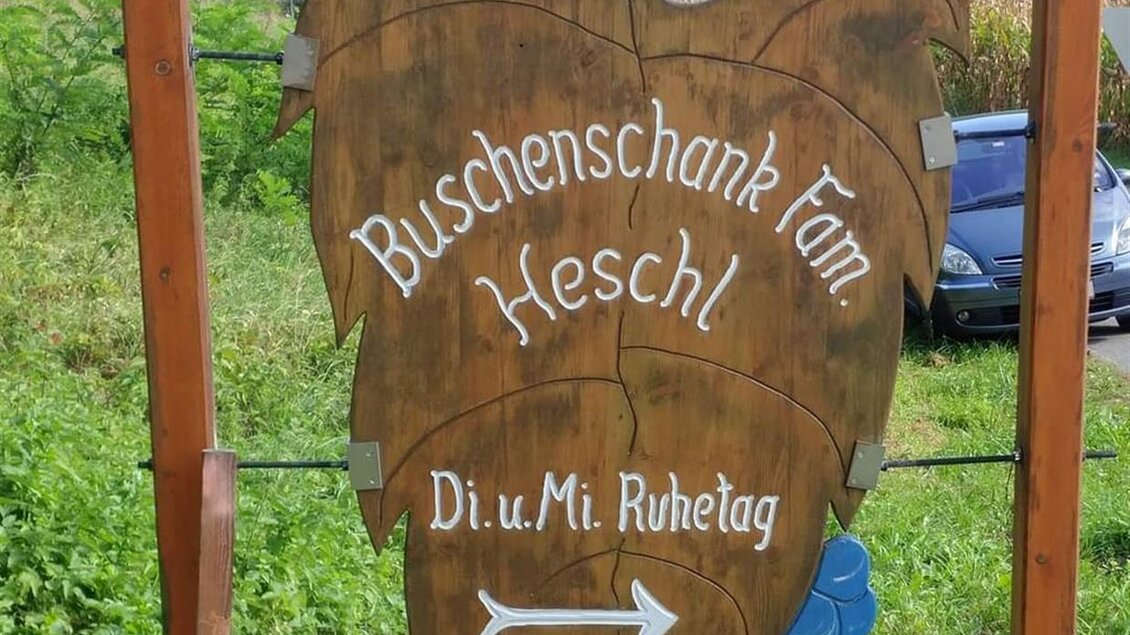 Ein Schild des Buscheschanks Fam. Heschl mit einer Weintraube als Symbol. Es zeigt die Öffnungszeiten und weist auf den Ruhetag hin. | © Buschenschank Heschl