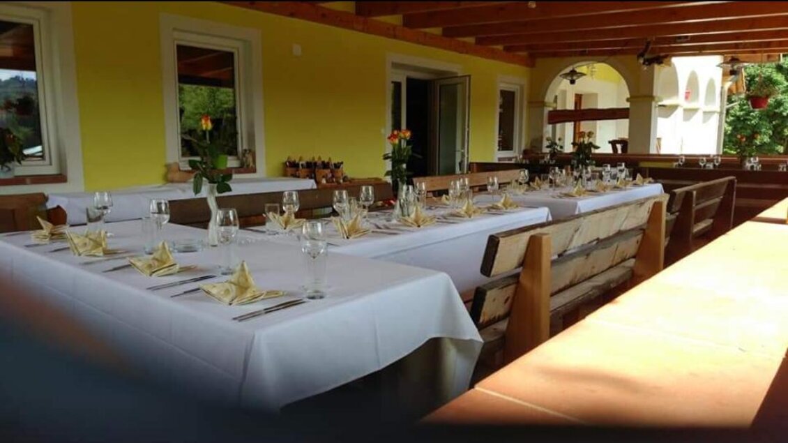 Ein gedeckter Tisch im Freien mit weißen Tischdecken und eleganten Gläsern. Die Umgebung ist hell und einladend, ideal für eine Feier. | © Buschenschank Heschl