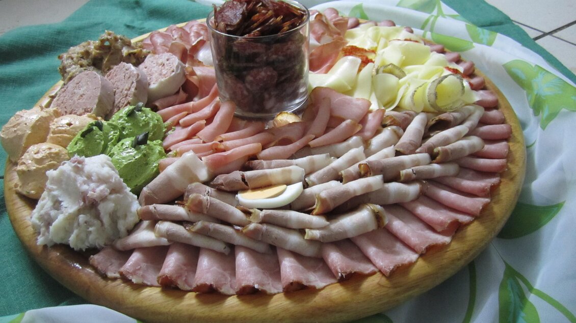 Ein reichhaltiges Käse- und Wurstbrett mit verschiedenen Aufschnittsorten, Ei und Salat. In der Mitte befindet sich ein Glas mit Trockenfrüchten. | © Weingut Holler