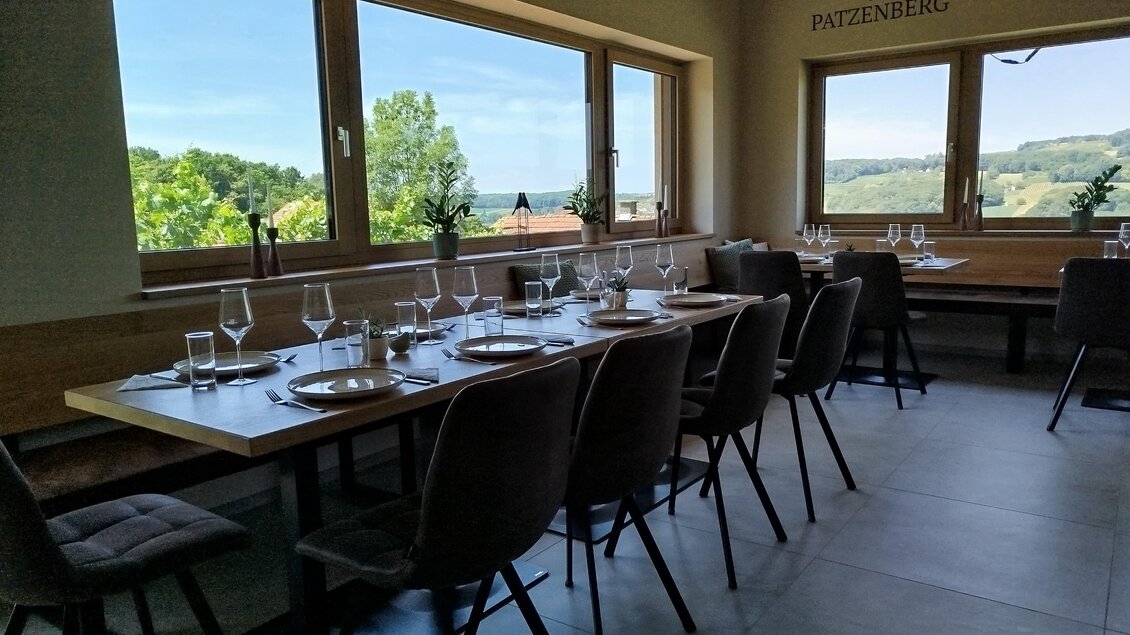 Ein modernes Restaurant mit großen Fenstern und Blick auf die grüne Landschaft. Der Tisch ist elegant gedeckt mit Gläsern und Geschirr.