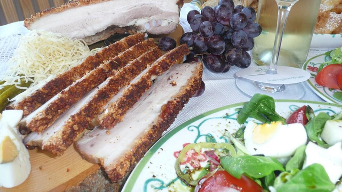 Ein leckerer Teller mit knusprigem Fleisch, frischen Trauben und einem bunten Salat. Dazu ein Glas Weißwein und einige Brotscheiben. | © Weingut Ilgi