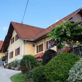 Ein charmantes Haus mit einem roten Satteldach und bunten Blumenkästen. Der gepflegte Garten und die ruhige Umgebung verleihen der Szene eine einladende Atmosphäre. | © Schilcherland Steiermark