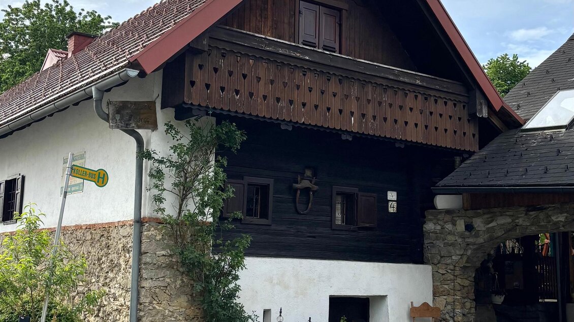 Ein traditionelles Haus mit einem schrägen Dach und Holzverzierungen. Die Fassade ist teilweise aus Stein, umgeben von grünen Pflanzen. | © Kraus-Ledinegg
