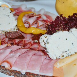 Ein köstliches Wurst- und Käsebrett mit verschiedenen Fleischsorten und frischen Beilagen. Attraktiv angerichtet mit Kräuterfrischkäse und buntem Gemüse.