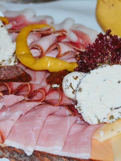 Ein köstliches Wurst- und Käsebrett mit verschiedenen Fleischsorten und frischen Beilagen. Attraktiv angerichtet mit Kräuterfrischkäse und buntem Gemüse.