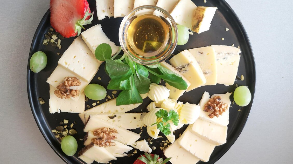 Ein ansprechend angerichteter Käse-Teller mit verschiedenen Käsesorten, Trauben und Erdbeeren. In der Mitte befindet sich ein Glas mit olivenöl und frischen Kräutern. | © Weingut & Buschenschank Stefanie Sauer