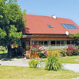 Ein gemütliches Holzhaus mit einem roten Dach und einem großen Garten. Blumen und Pflanzen umgeben das Haus, und es gibt einen blauen Himmel. | ©  Buschenschank Schulter