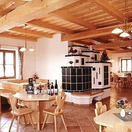 Ein gemütliches Restaurant mit Holzdecke und warmem Ambiente. Tische sind eingedeckt und eine Kachelofen sorgt für eine einladende Atmosphäre. | © Weinhof Tauchmann