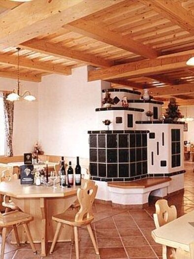 Ein gemütliches Restaurant mit Holzdecke und warmem Ambiente. Tische sind eingedeckt und eine Kachelofen sorgt für eine einladende Atmosphäre. | © Weinhof Tauchmann